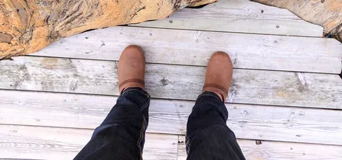 Person wearing brown boots standing on a weathered whitewashed wooden floor with a Scandinavian-style finish.