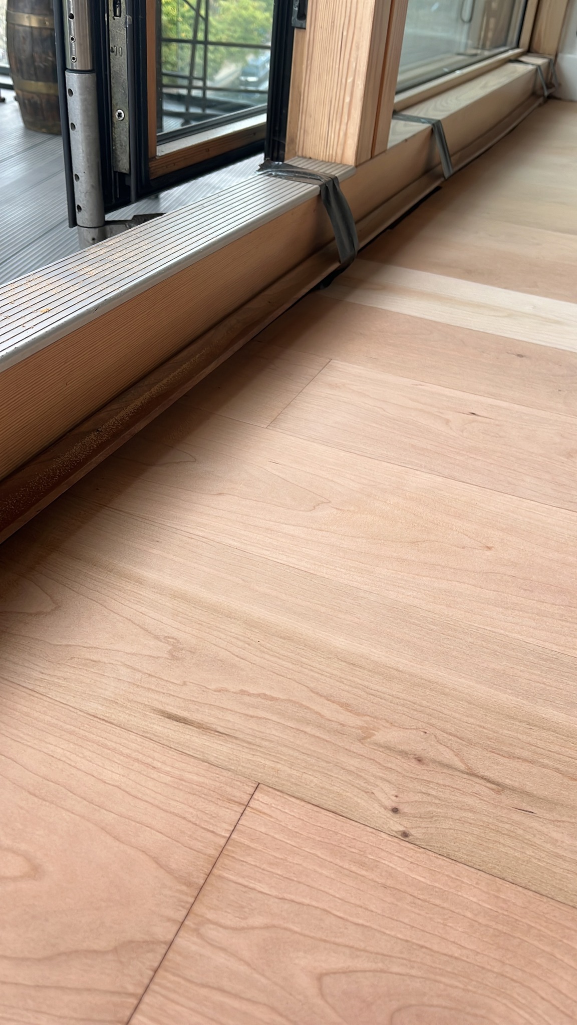 Bare sanded hardwood floorboards beside a balcony sliding door frame, with tape on the frame