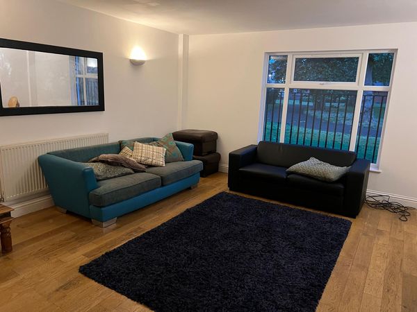 Furnished living room with oak plank flooring, two sofas, a navy shag rug and a large window onto a green.