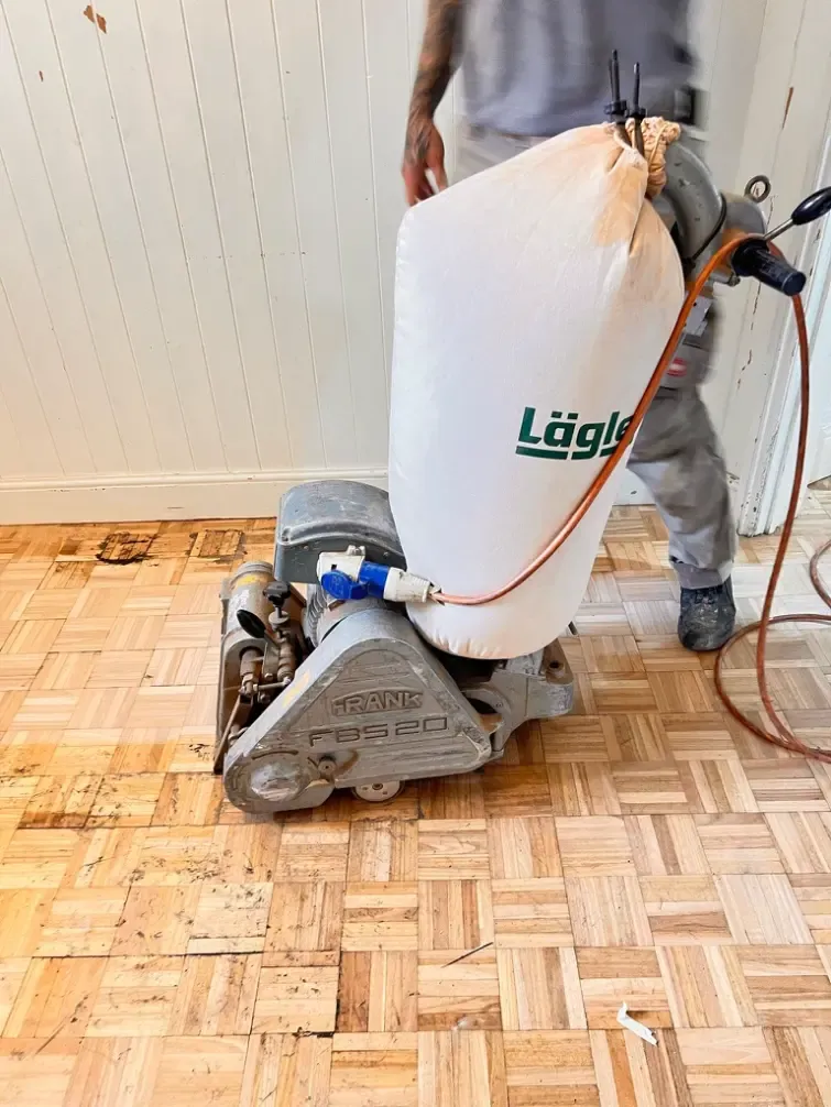Dust-free floor sanding machine with dust collection bag sanding a parquet timber floor indoors.