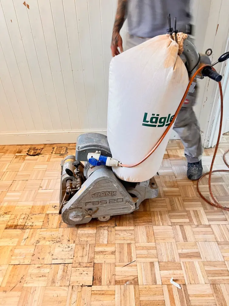 Dust-free floor sanding machine with dust collection bag sanding a parquet timber floor indoors.