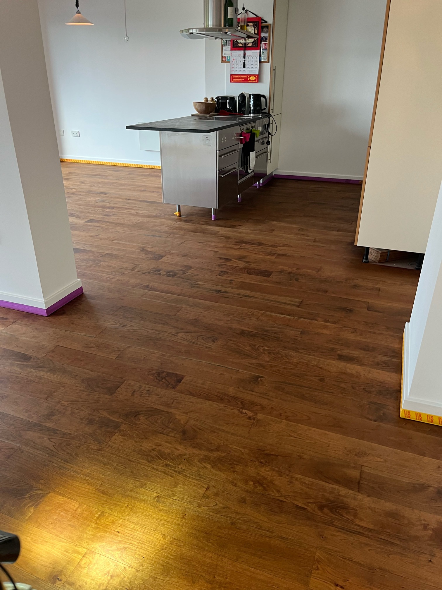 Dark brown hardwood floor in front of a kitchen island with a purple-taped column in the foreground