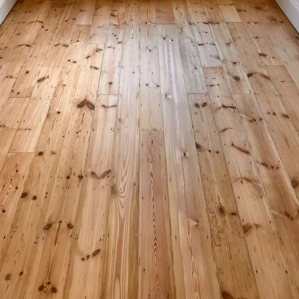 Restored pine floorboards in a bright London bedroom, showing seamless repair, gap filling, and sanding results