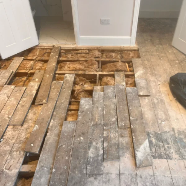 Exposed timber floor with lifted boards, visible joists, and insulation during a floorboard repair project in London