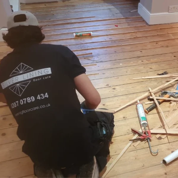Floor restoration specialist filling gaps in Victorian pine floorboards using reclaimed wood slivers