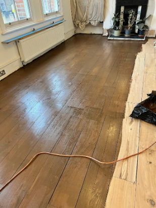 Partially stained wood floor showing the difference between bare sanded boards and the darker tone created by stain during a restoration process.