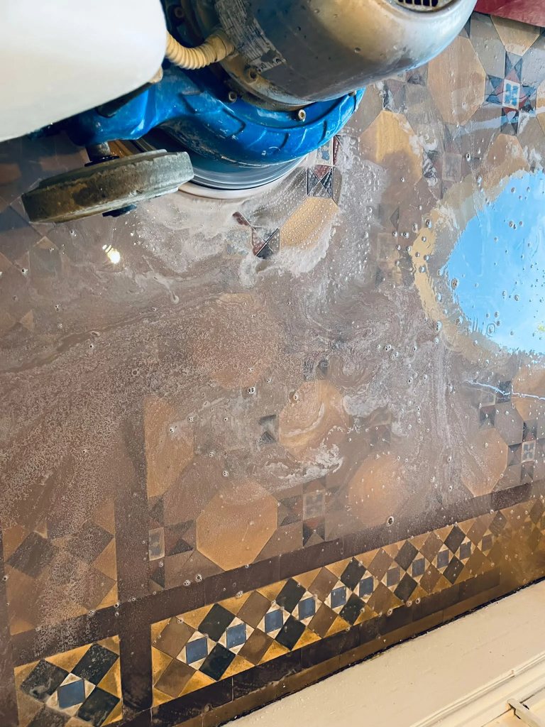 Specialist cleaning of Victorian tiles in London using a professional cleaning machine, showcasing bubbles and a cleaning solution over intricate tile patterns
