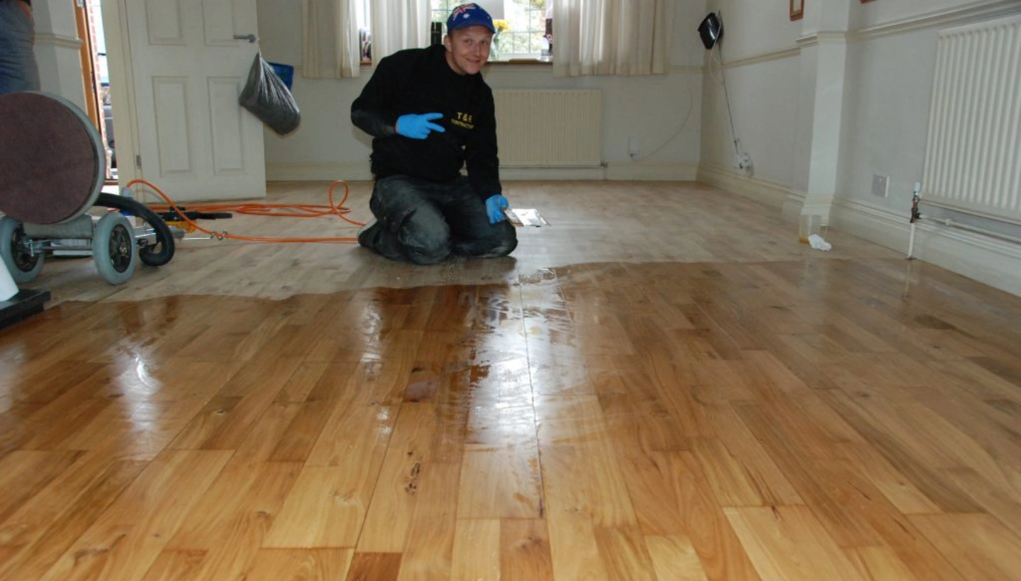 A floor restoration expert applying Magic Oil 2K on an oak floor in Pratts Bottom, South London. The image captures the transformation process, with half of the floor sanded and oiled, contrasting with the worn, scratched surface.