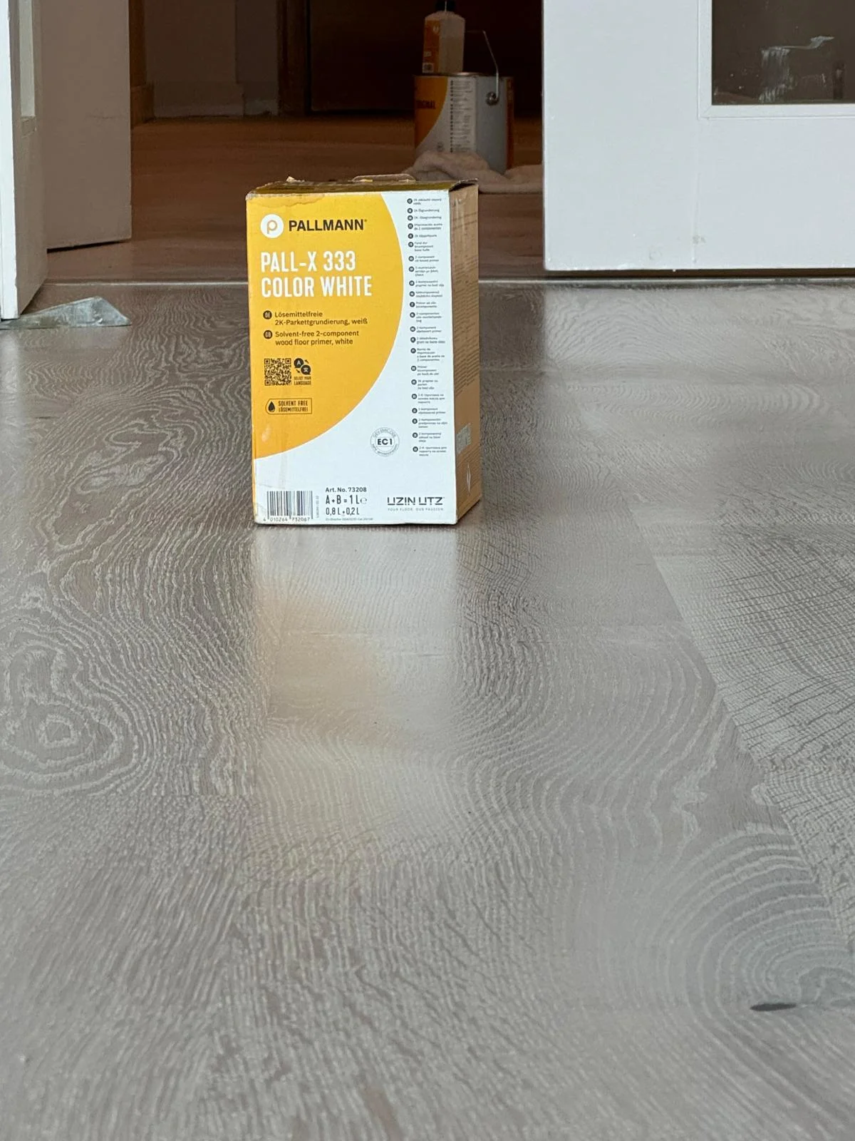 Box of Pallmann Pall-X 333 Color White placed on a Scandinavian-finished wood floor, showcasing a light, airy effect with visible grain.