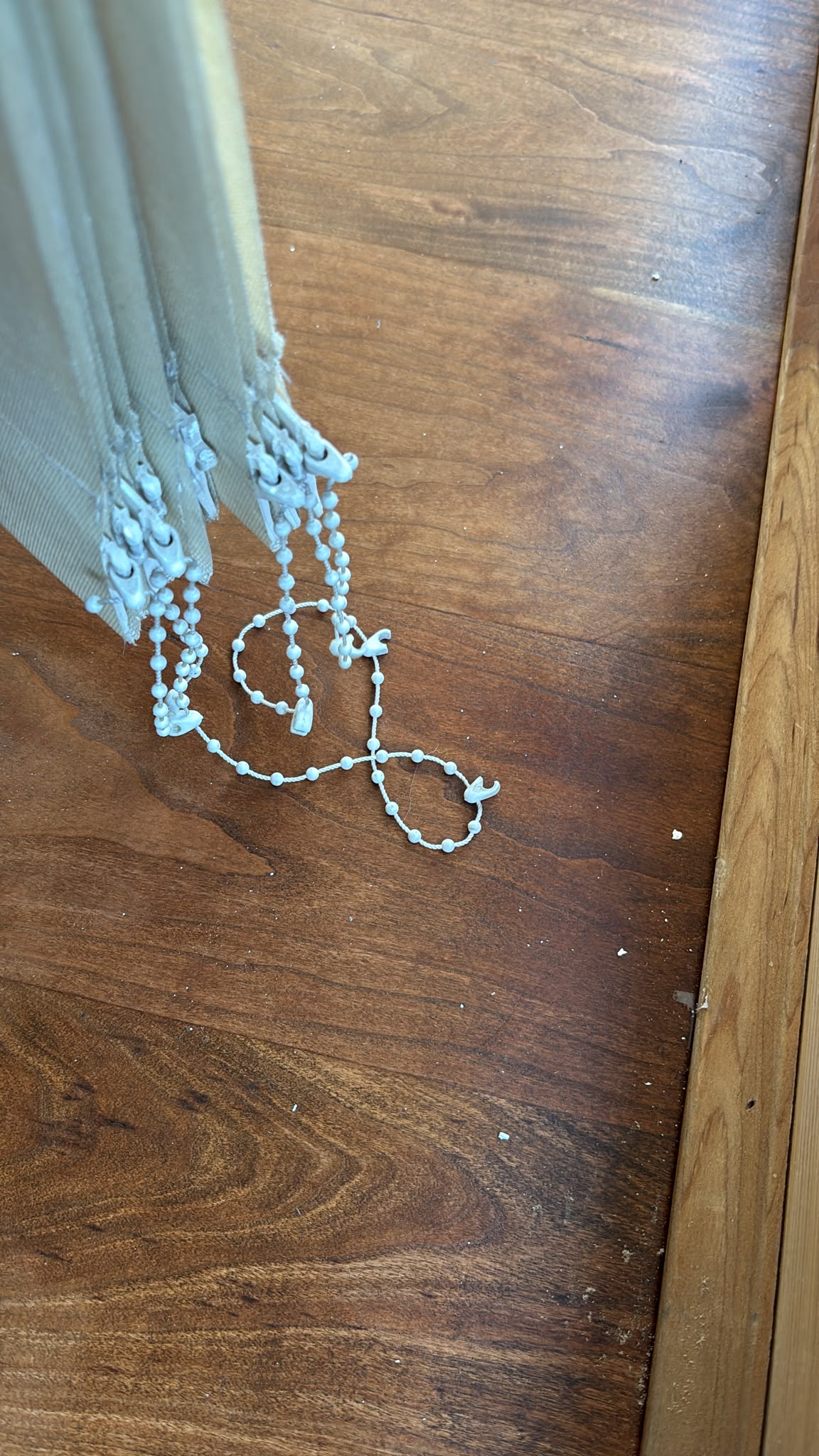 Dark hardwood floor beside a wooden threshold, with white blind cords resting on the boards