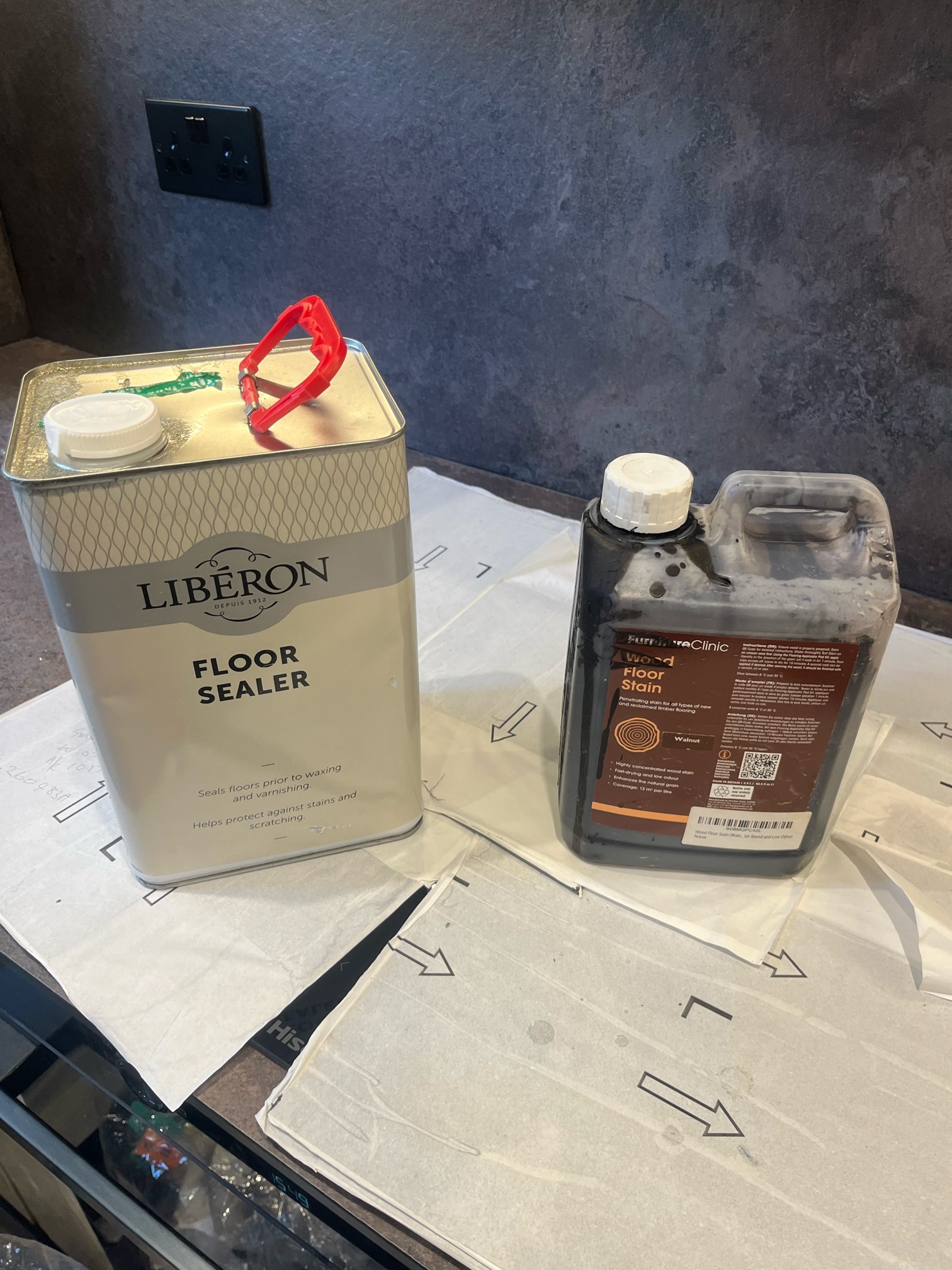 A tin of Liberon Floor Sealer next to a container of Furniture Clinic Wood Floor Stain in Walnut, on dust sheets.