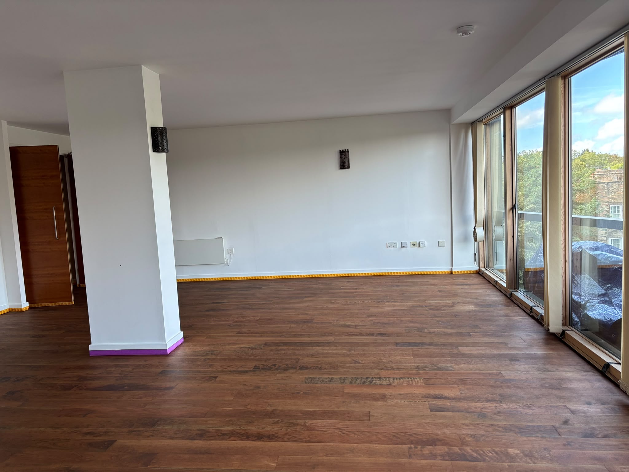 Empty open-plan living room with a freshly finished dark brown hardwood floor and floor-to-ceiling windows