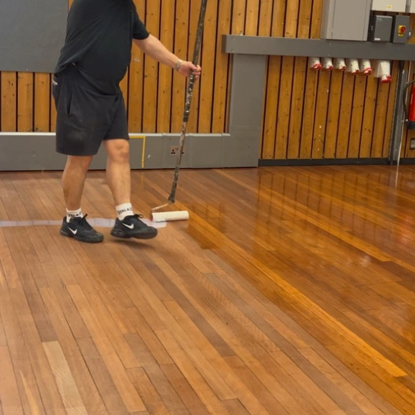 Expert applying varnish to a wooden floor using a roller, ensuring a smooth and even finish for long-lasting protection.