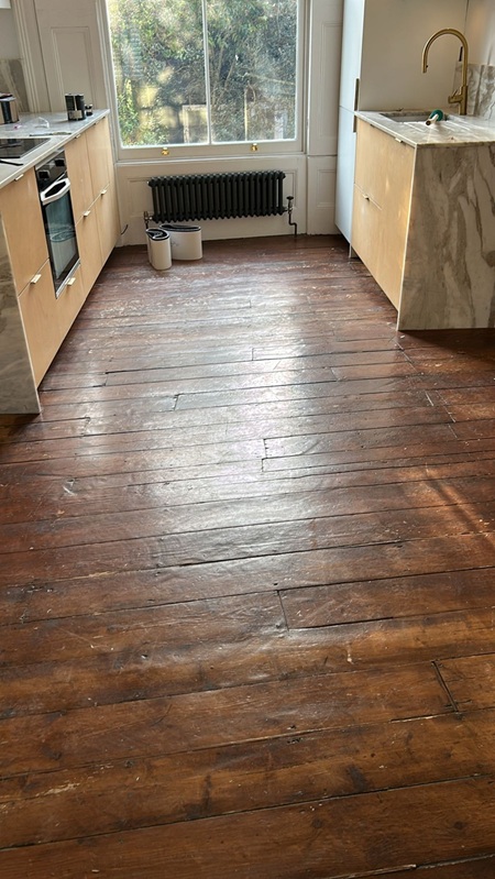 Victorian pine floorboards in London kitchen before restoration showing worn dark varnish and heavy wear