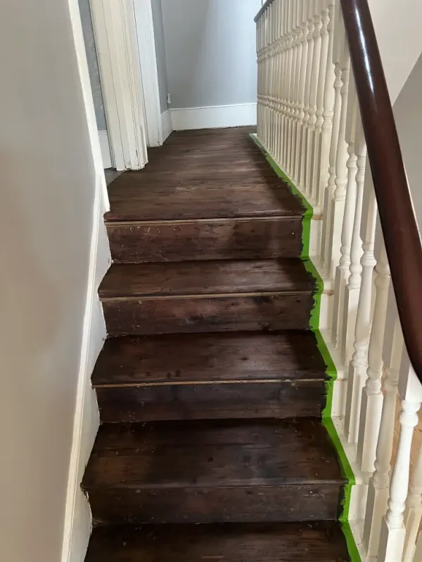 Before photo of a staircase and wood floor renovation in a London home, showing the original dark timber stairs and painted spindles.