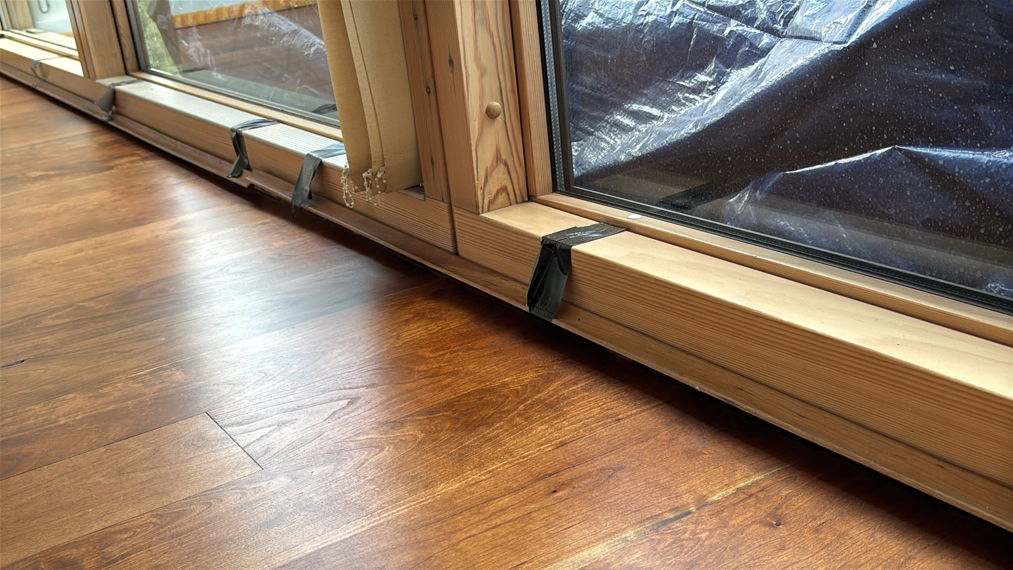 Glossy lacquered hardwood floor meeting a wooden sliding door frame, with black tape on the frame