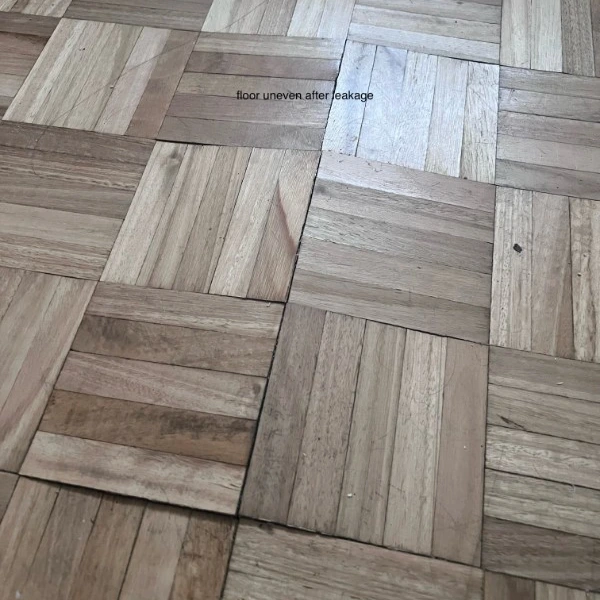 Uneven parquet flooring damaged by water leakage, showing warping and discoloration.