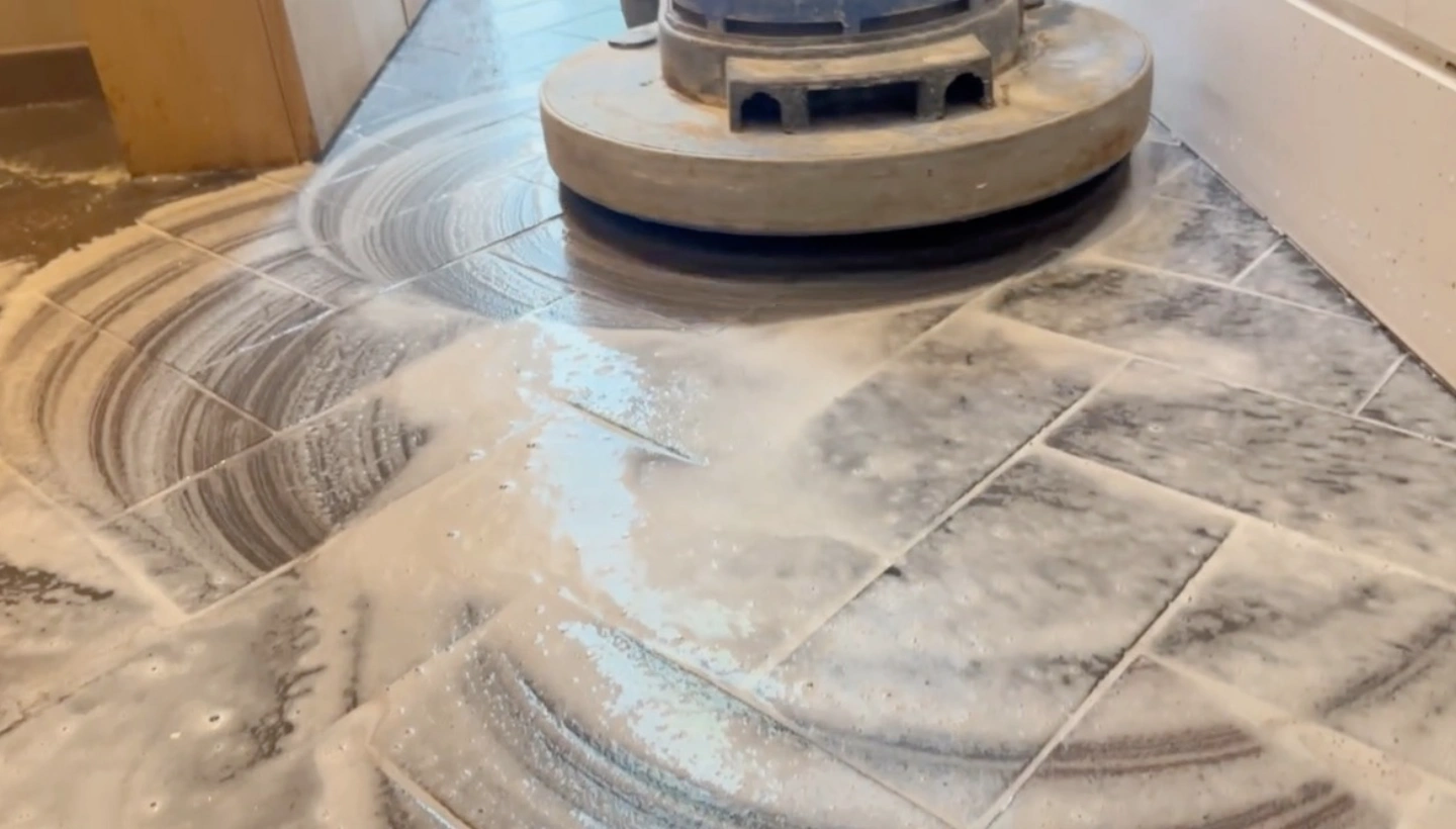 In-progress cleaning of blue brick ceramic tiles with a rotary floor machine and detergent