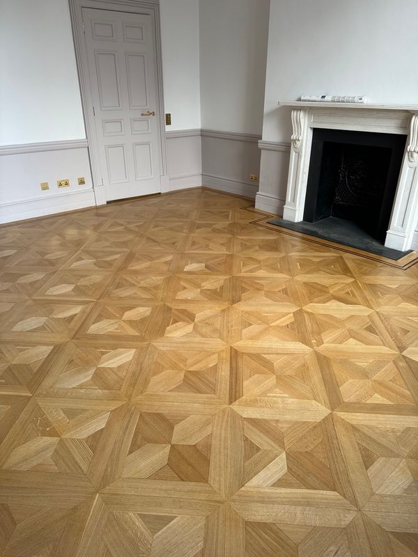 Restored geometric parquet floor in a London period room with a marble fireplace.