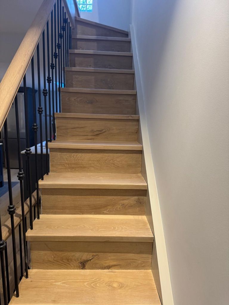 Refinished oak staircase after stair sanding, featuring black iron balusters and a natural wood handrail in London.