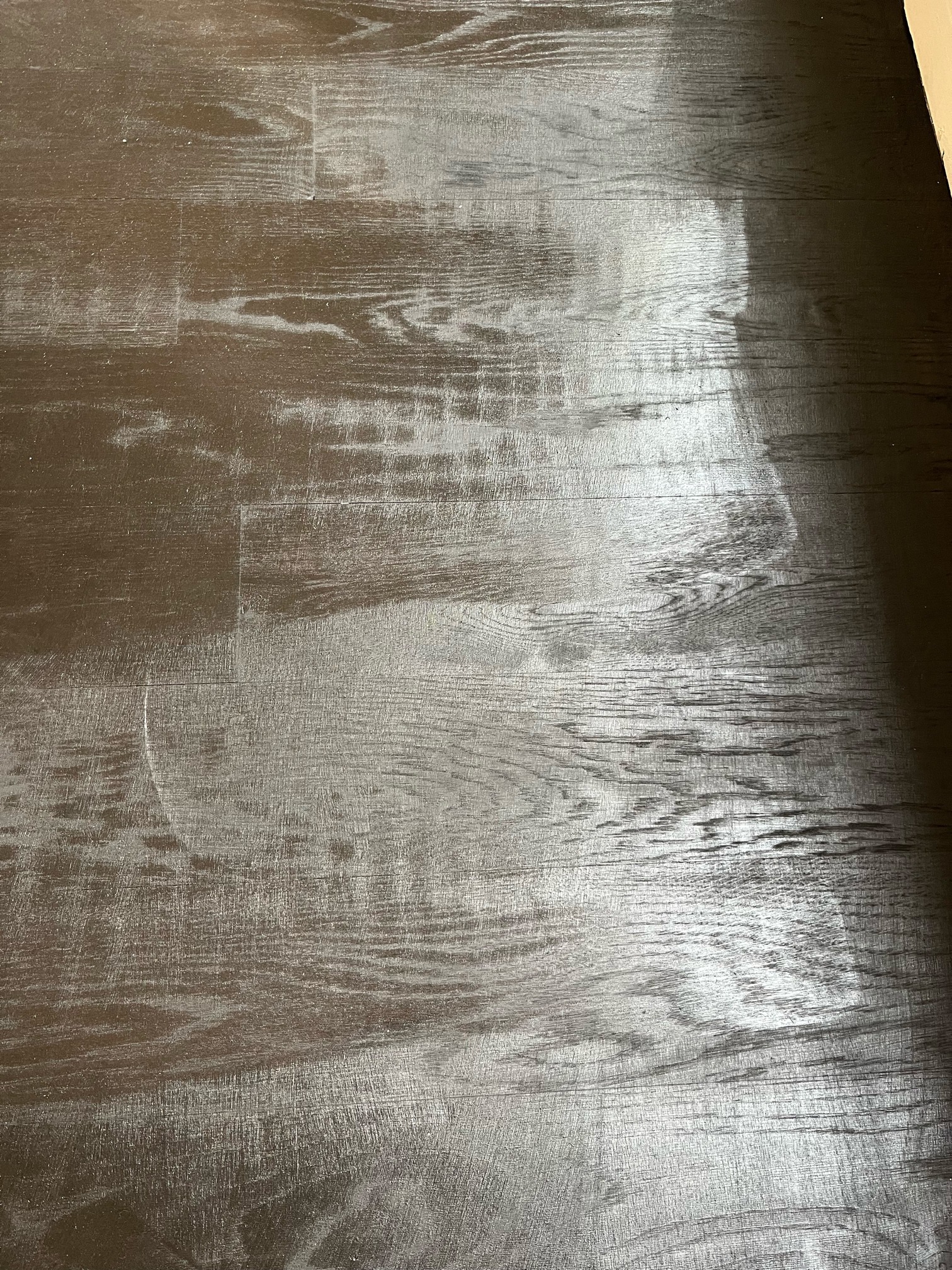 Overhead view of dark stained oak boards with streaky light and dark patches and a faint curved mark across one board.