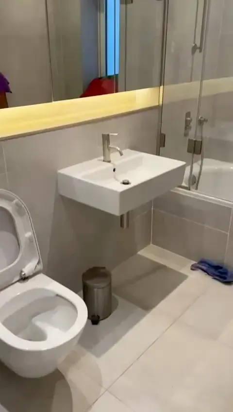 Modern bathroom with wall-mounted sink, toilet, bathtub with glass shower screen, and tiled floor.