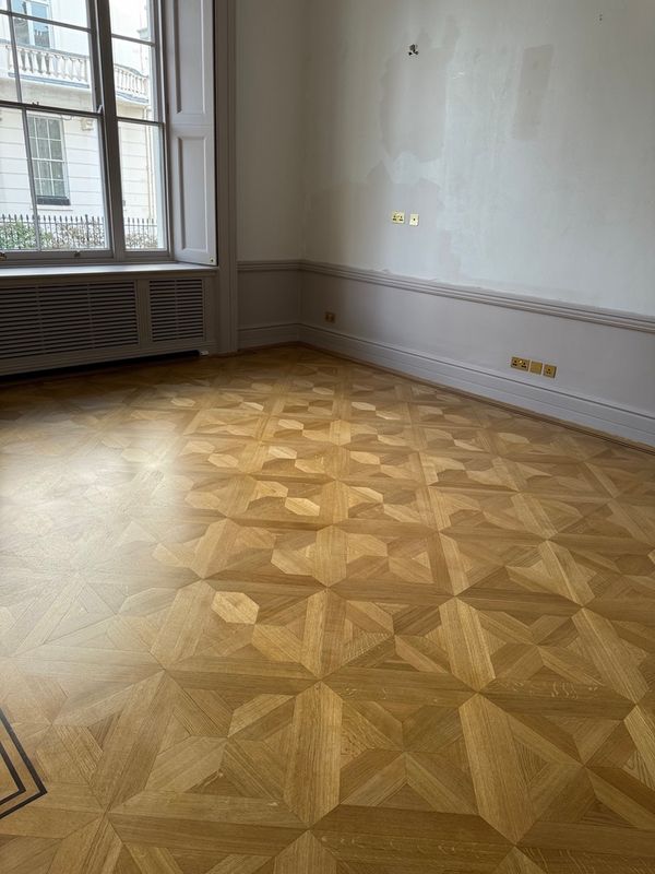 Restored geometric parquet wood floor in a London period property, with sash windows and original wall paneling visible.