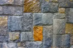 Close-up of an outdoor stone wall with visible discoloration, moss, and rust stains, highlighting the need for professional stone cleaning and restoration.