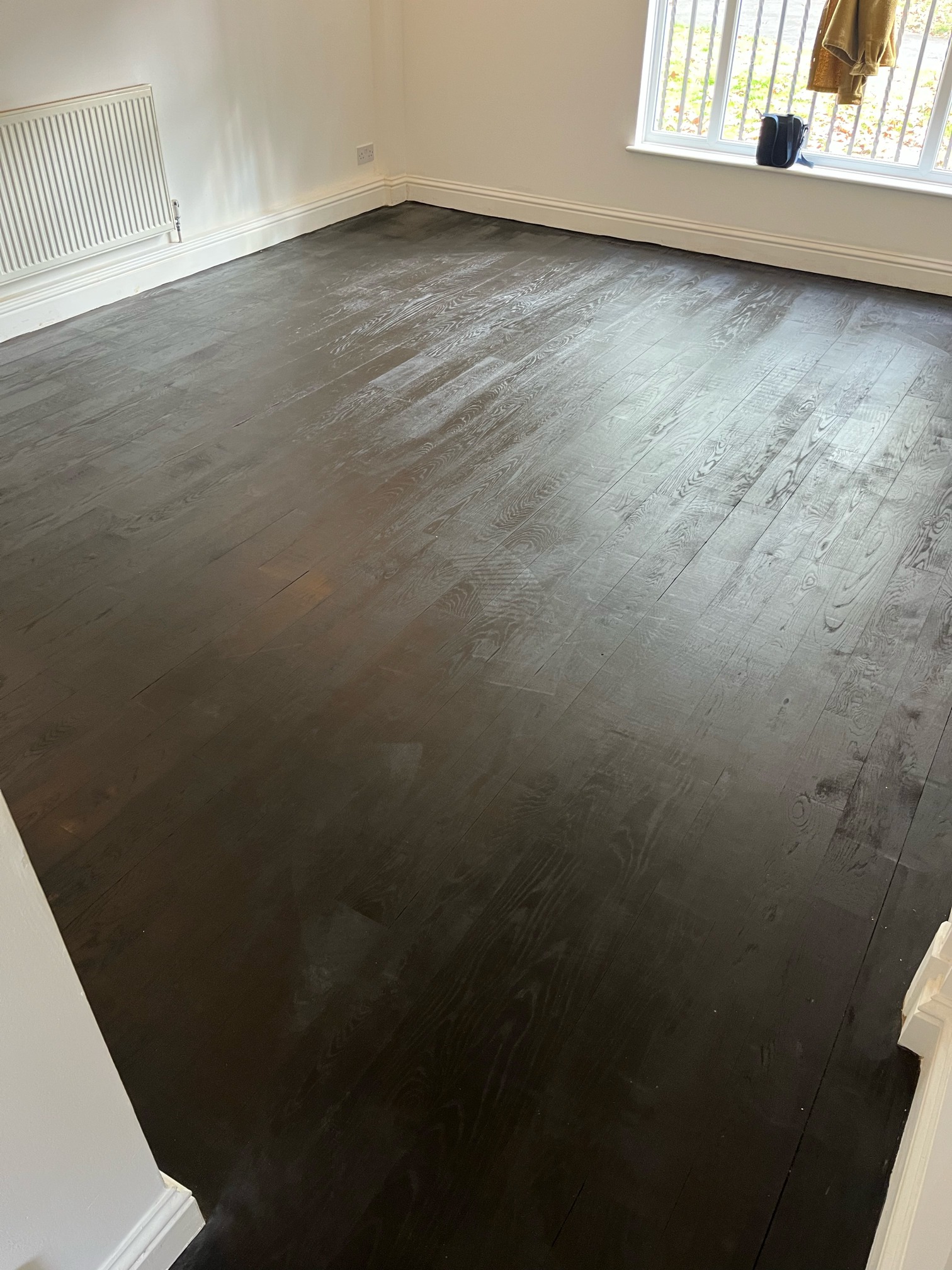 Empty room with oak flooring stained dark walnut, showing lighter patches and visible grain under daylight.