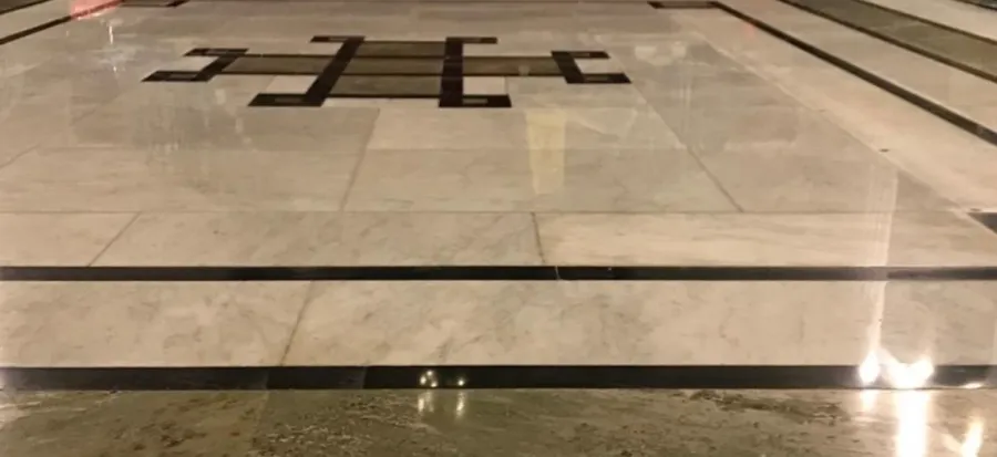 Close-up of a polished natural stone floor with dark inlay, demonstrating proper cleaning and care techniques.