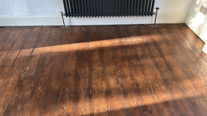 Original pine floorboards in London home before restoration with sunlight highlighting worn finish