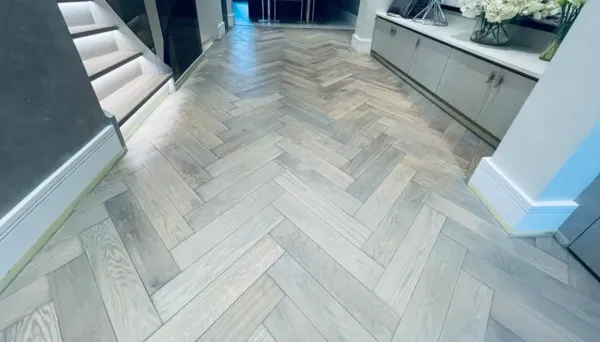 A beautifully restored oak floor in Kensington, London, stained in a custom grey shade with a herringbone pattern, enhancing the elegance of the space.