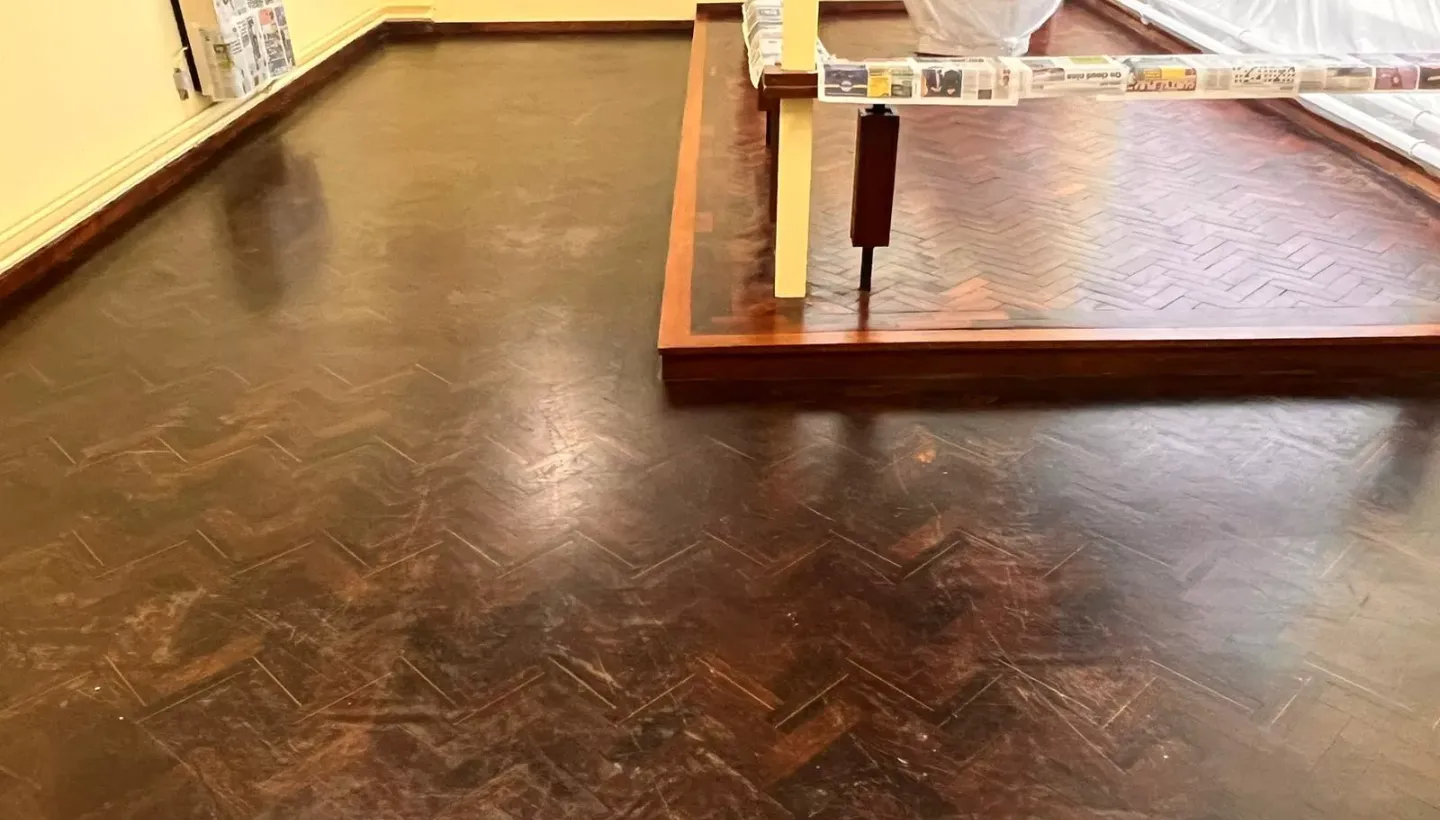 Scratched and dull tropical hardwood floor with heavy lacquer wear in Heston church before sanding and refinishing