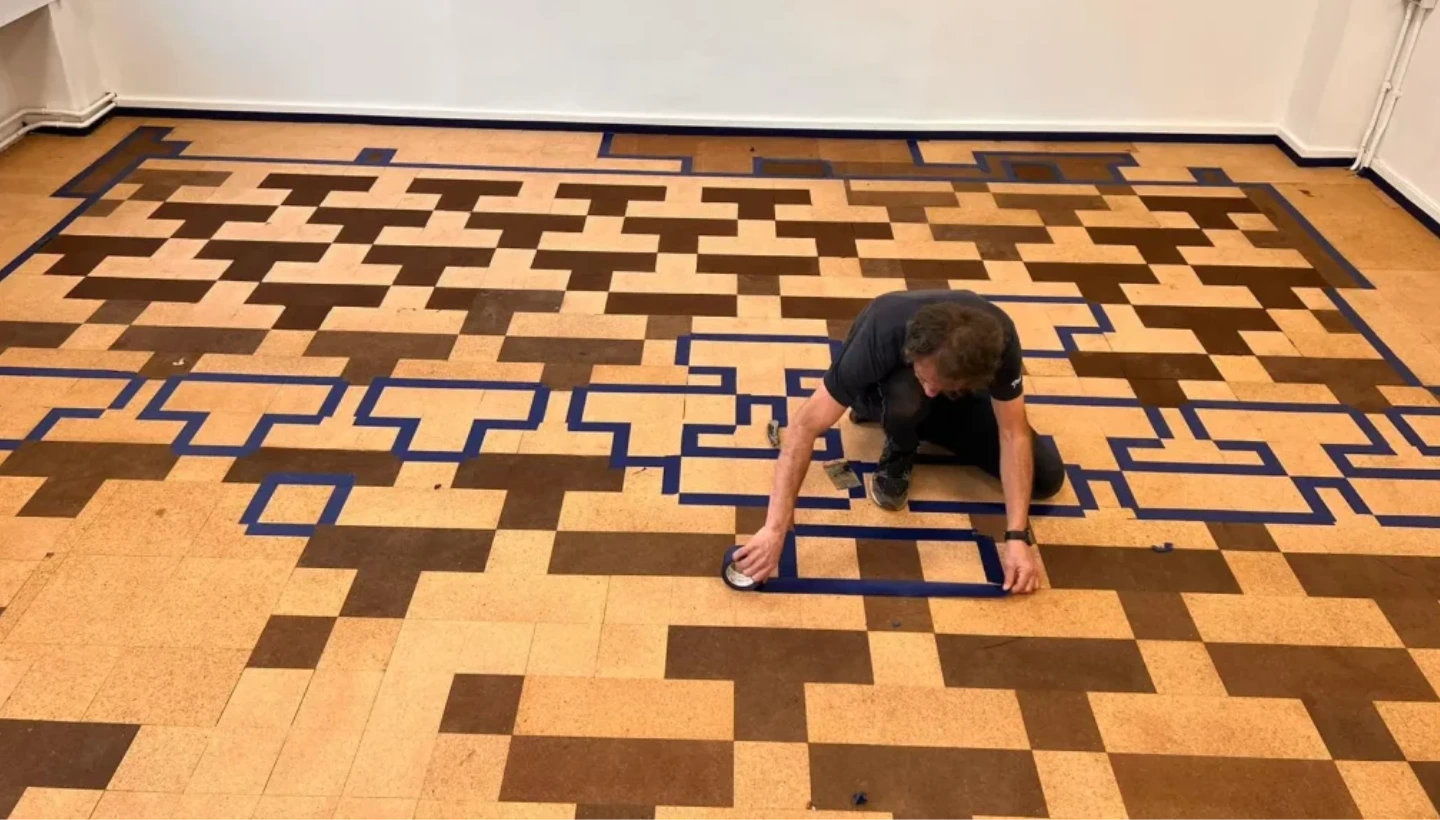 A professional applying tape to a cork floor in a London school, preparing for precise sanding and staining to match the original pattern.