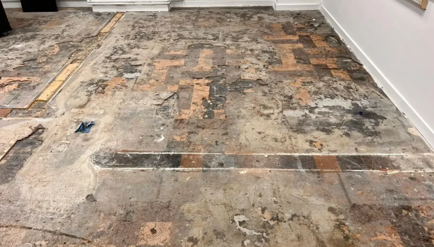 Heavily worn and damaged cork flooring in a London school before restoration, showing missing sections and deterioration.