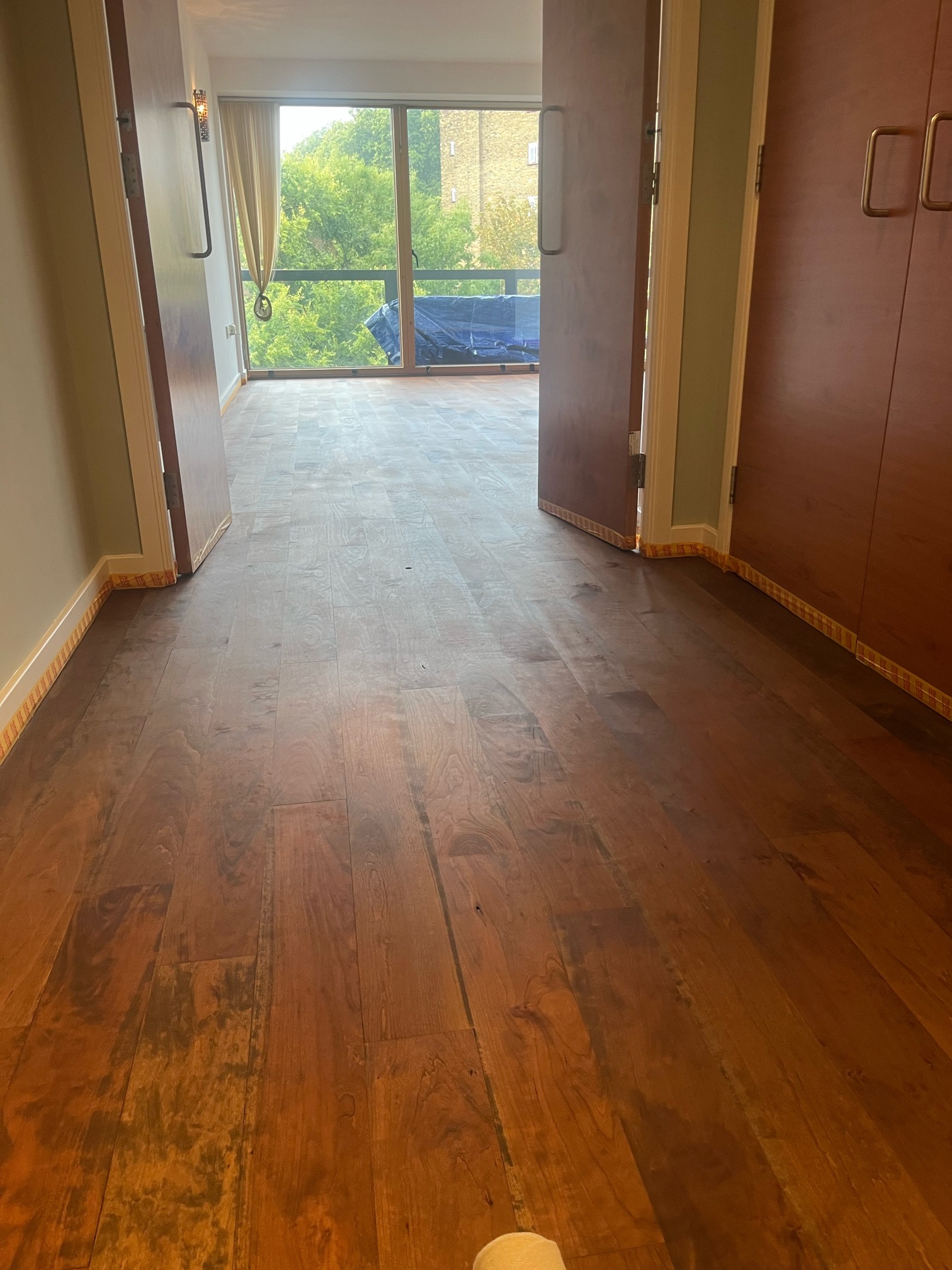 Hallway hardwood floor with uneven, patchy colour leading to double doors and a balcony window