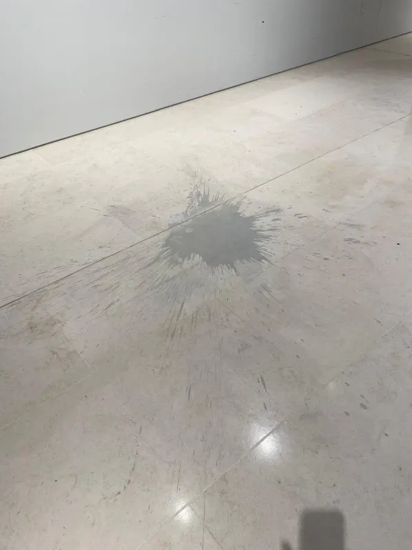 Acid etching damage on a natural stone floor caused by a liquid spill, showing a dull etched patch on stone tiles