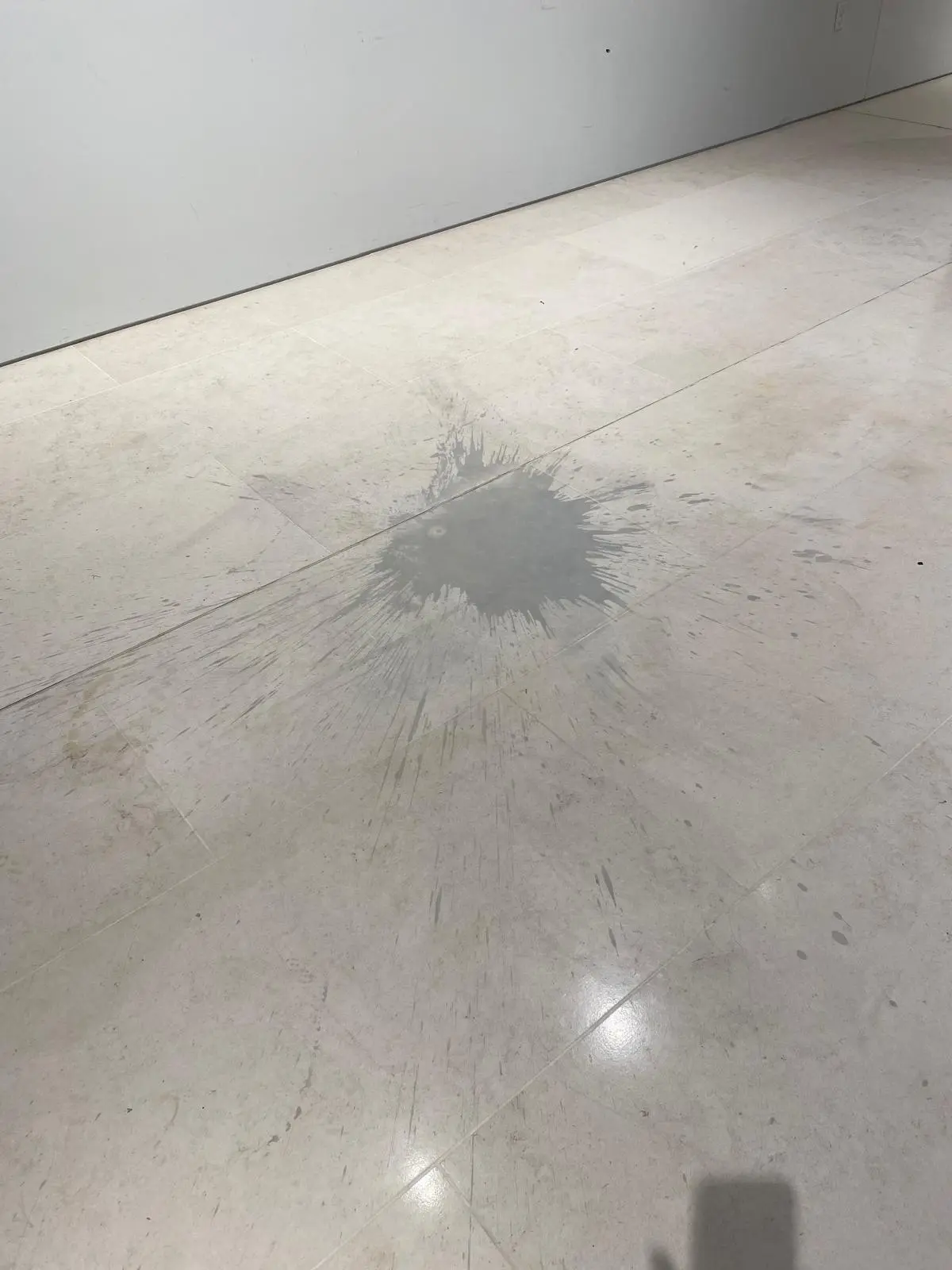 Acid etching damage on a natural stone floor caused by a liquid spill, showing a dull etched patch on stone tiles