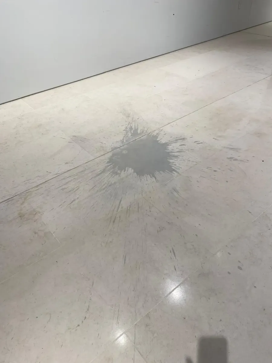 Acid etching damage on a natural stone floor caused by a liquid spill, showing a dull etched patch on stone tiles