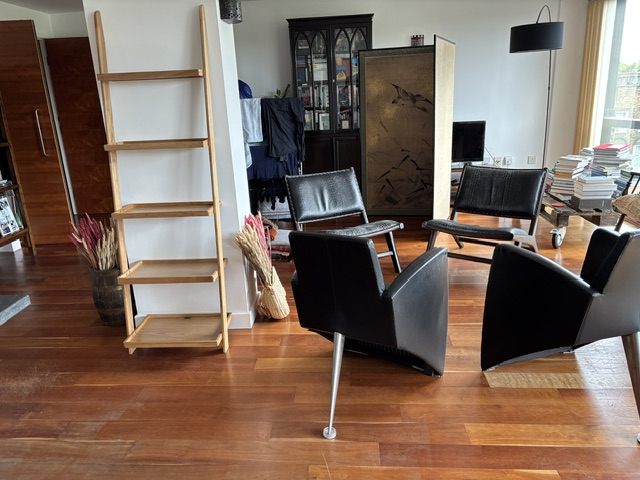 Reddish-brown hardwood floor in a furnished living room with black leather armchairs and a bookcase