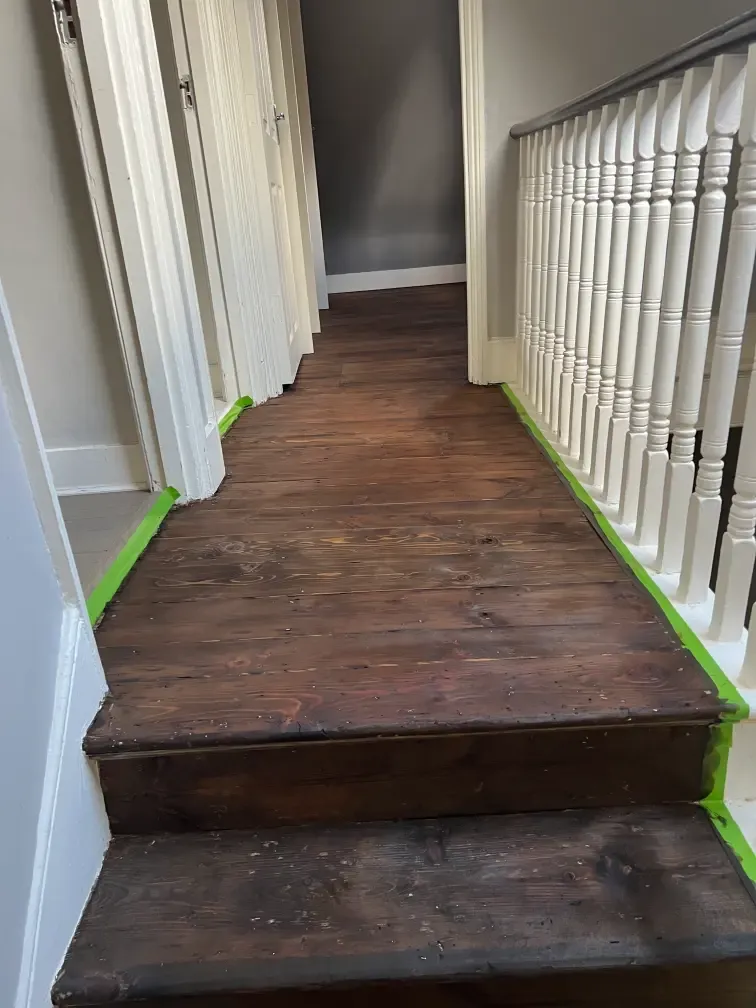 London staircase landing before wood floor and stair renovation, with dark timber boards and white balustrade.