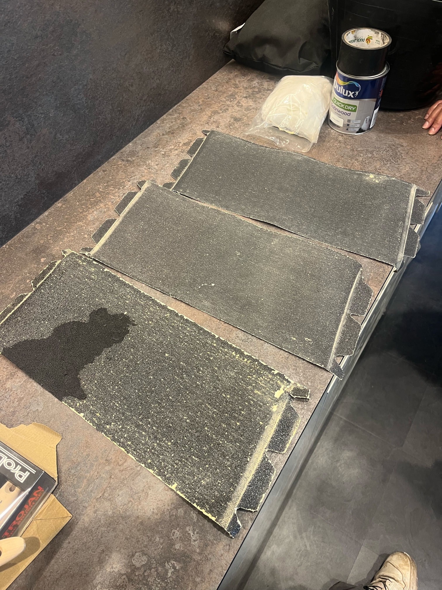 Three used floor sanding sheets laid side by side on a worktop, the coarsest one clogged with stain and dust.
