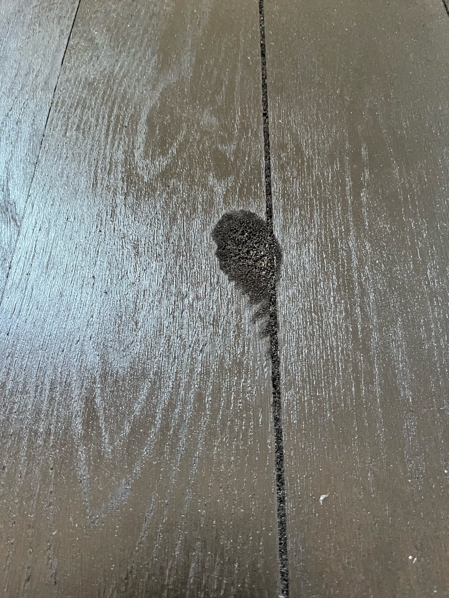 Close-up of a dark, porous blotch on stained oak boards beside an open joint.