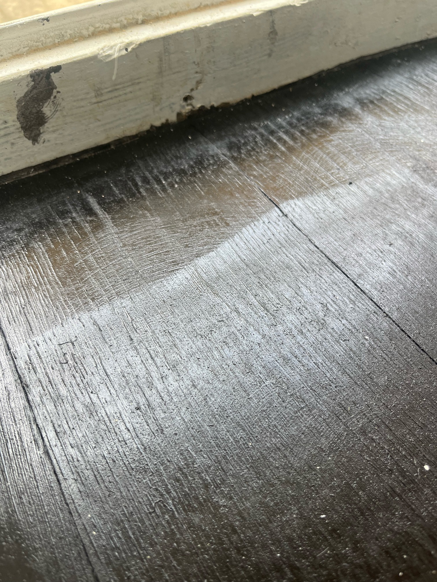 Close-up of dark walnut stain on oak planks beside a worn white door threshold, with uneven, patchy colour.