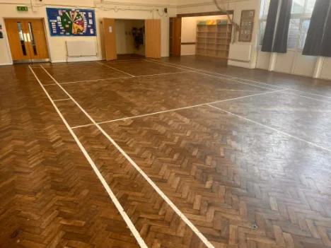 Worn parquet school hall floor with white sports court markings, awaiting sanding and restoration in Caterham.