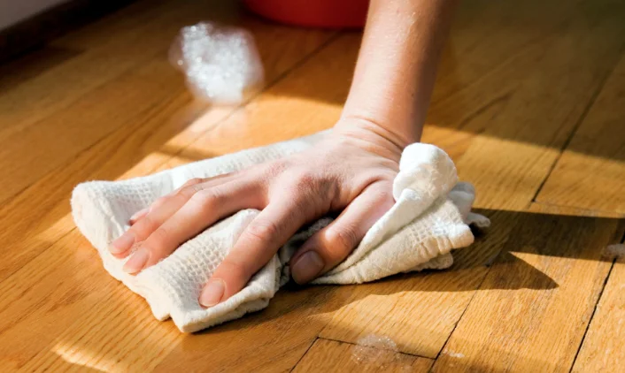 hand wiping the wooden floor with a towel